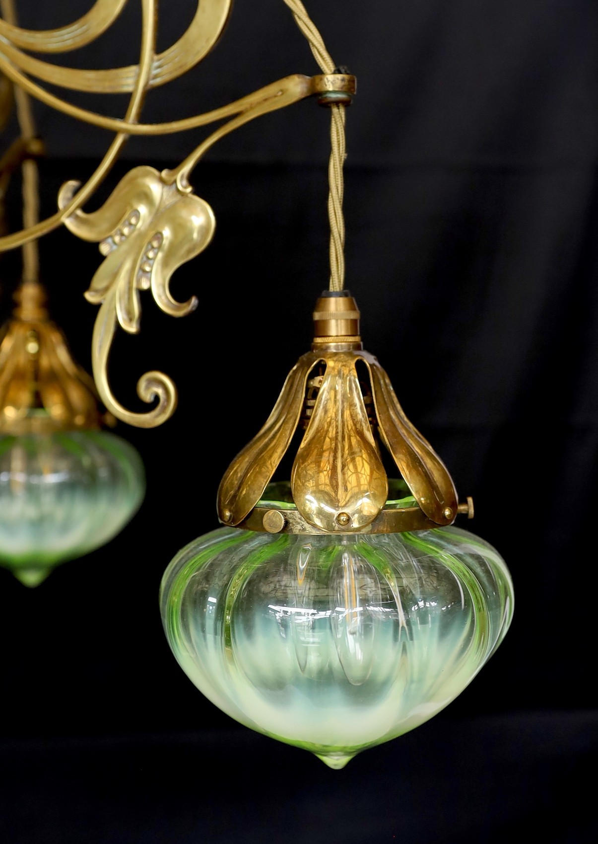 An English Arts & Crafts brass light fitting with scrolling foliate branches and tinted iridescent glass shades, height 68cm. width 46cm